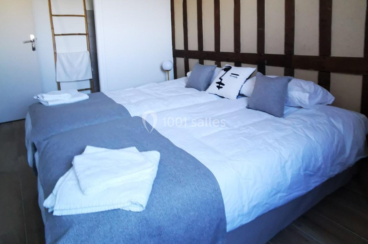 Lit double avec draps blancs, couvertures grises, oreillers assortis et serviettes pliées dans une chambre lumineuse.