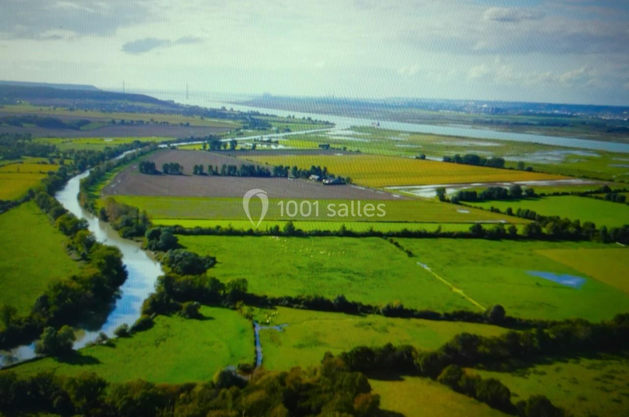 Vue aérienne d'une campagne verdoyante avec des champs, un cours d'eau sinueux et un horizon dégagé.