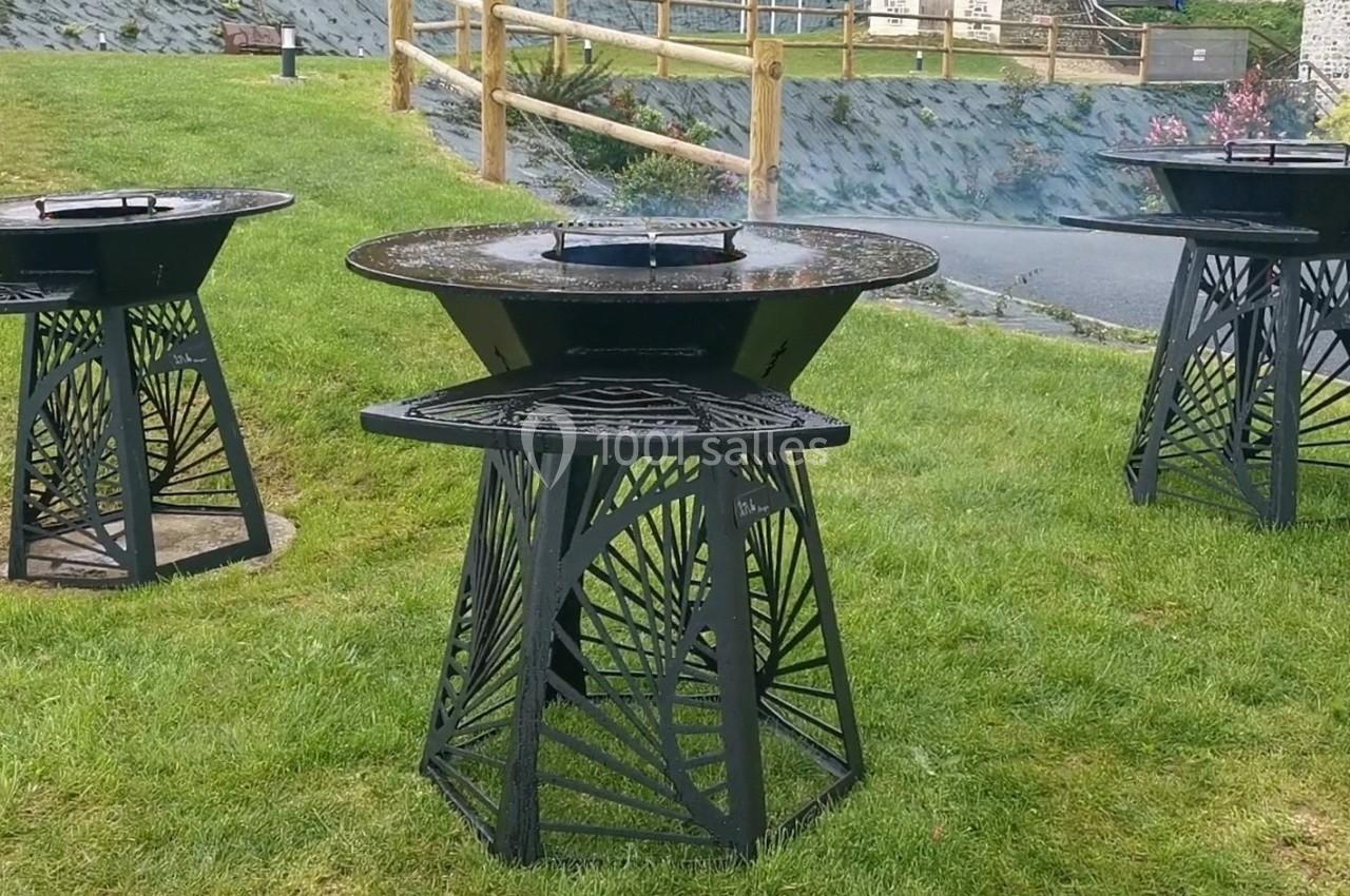 Trois barbecues en métal noir au design ajouré, installés sur une pelouse dans un espace extérieur.