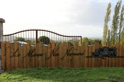 Aire de jeux en bois sur sol sablonneux, entourée de verdure et située près de bâtiments ruraux sous un ciel bleu.