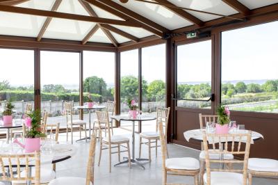 Aire de jeux en bois sur sol sablonneux, entourée de verdure et située près de bâtiments ruraux sous un ciel bleu.
