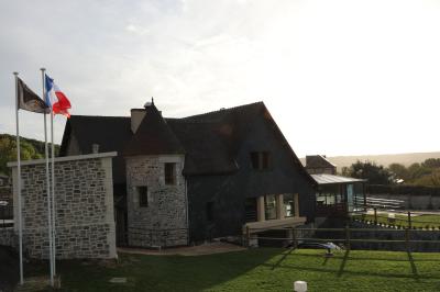 Aire de jeux en bois sur sol sablonneux, entourée de verdure et située près de bâtiments ruraux sous un ciel bleu.