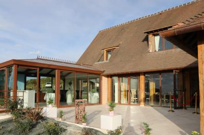Aire de jeux en bois sur sol sablonneux, entourée de verdure et située près de bâtiments ruraux sous un ciel bleu.
