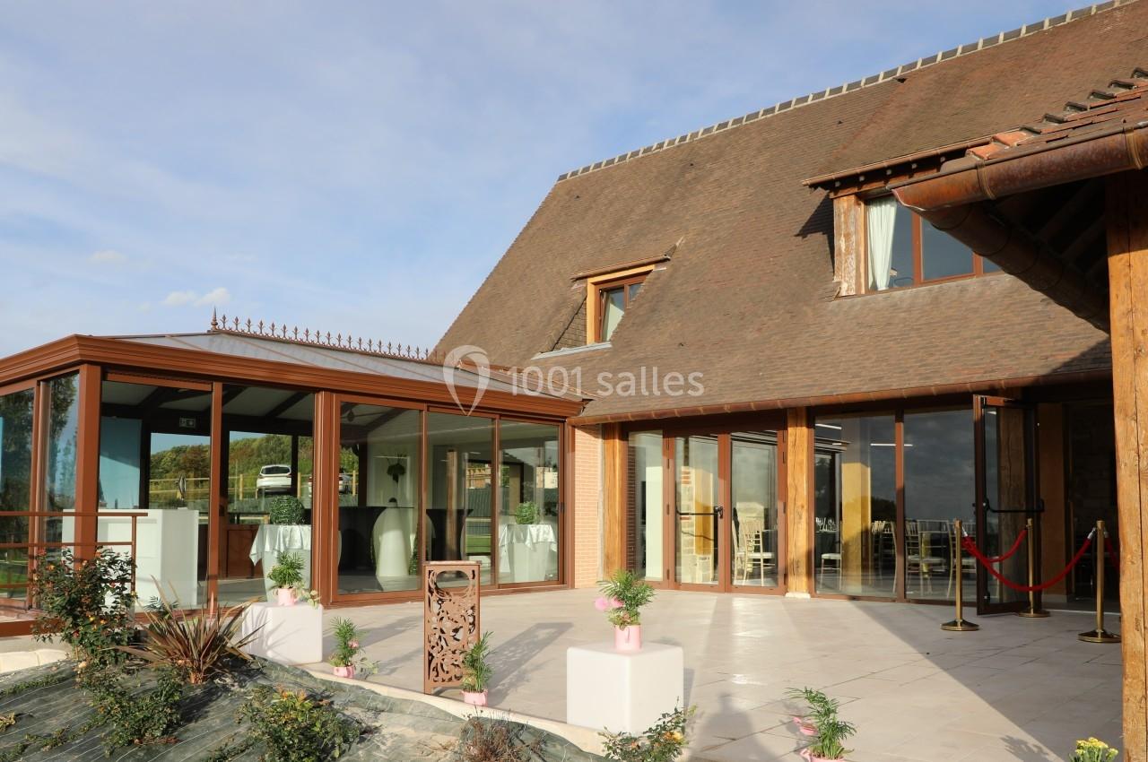 Façade d'un bâtiment avec une véranda vitrée, des plantes en pot et une entrée décorée de rubans rouges.