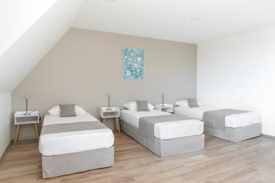 Aire de jeux en bois sur sol sablonneux, entourée de verdure et située près de bâtiments ruraux sous un ciel bleu.