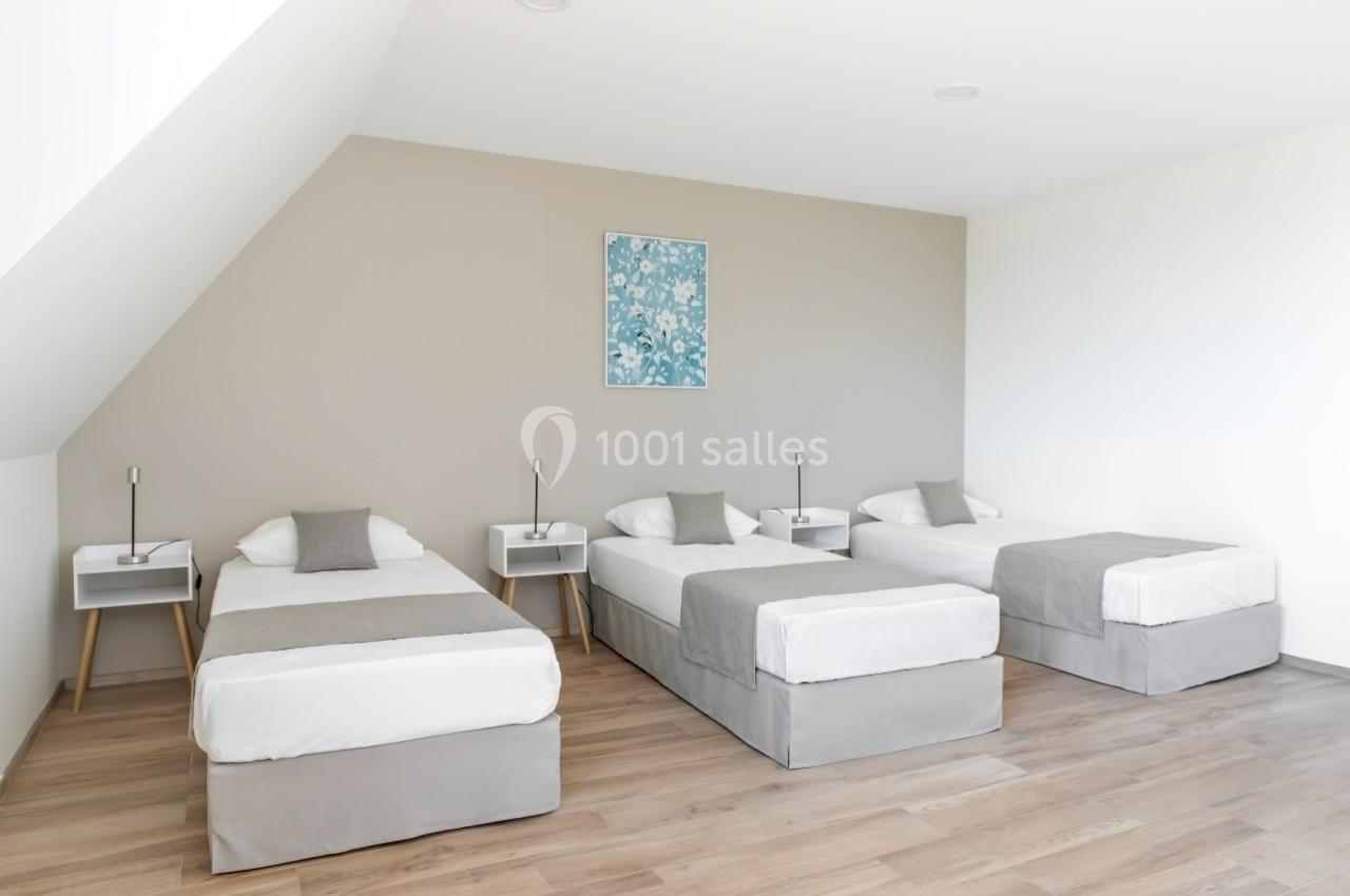 Trois lits simples alignés dans une chambre lumineuse avec parquet, murs clairs et tableau décoratif.