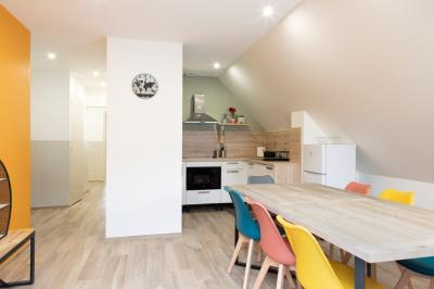 Aire de jeux en bois sur sol sablonneux, entourée de verdure et située près de bâtiments ruraux sous un ciel bleu.