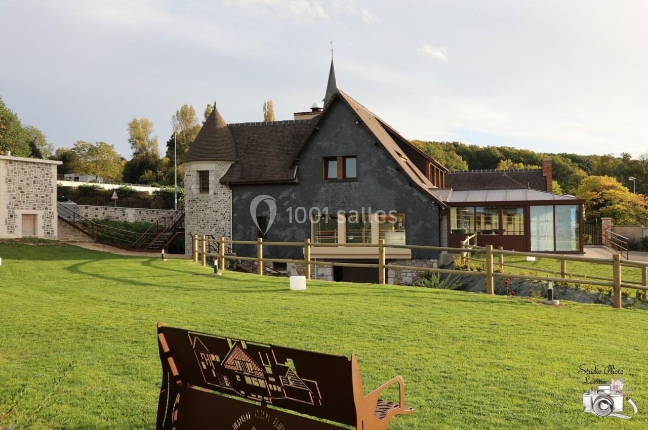 Bâtiment en pierre et ardoise avec une tour, entouré d'un jardin verdoyant et d'une clôture en bois.