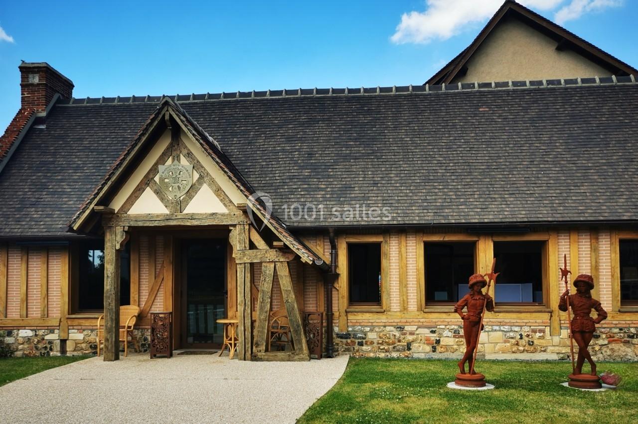 Façade d'une maison à colombages avec toit en ardoise, statues décoratives et jardin bien entretenu au premier plan.