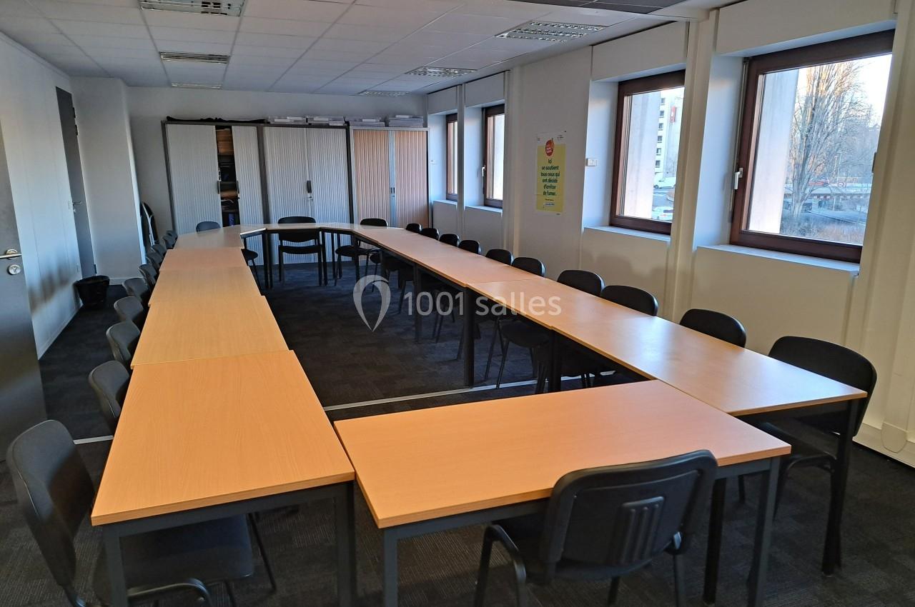 Salle de réunion avec tables disposées en U, chaises noires, fenêtres laissant entrer la lumière naturelle.