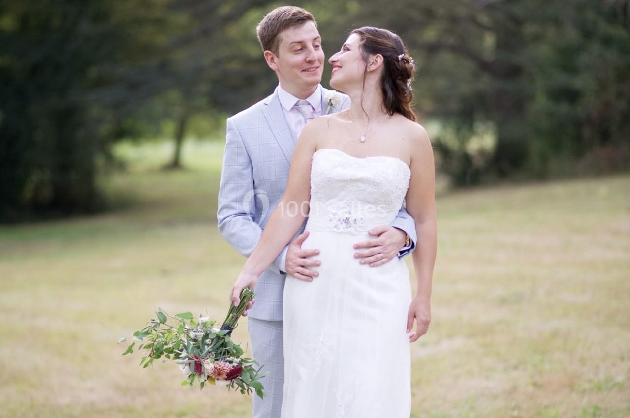 Un couple en tenue de mariage pose dans un parc, la mariée tenant un bouquet de fleurs.
