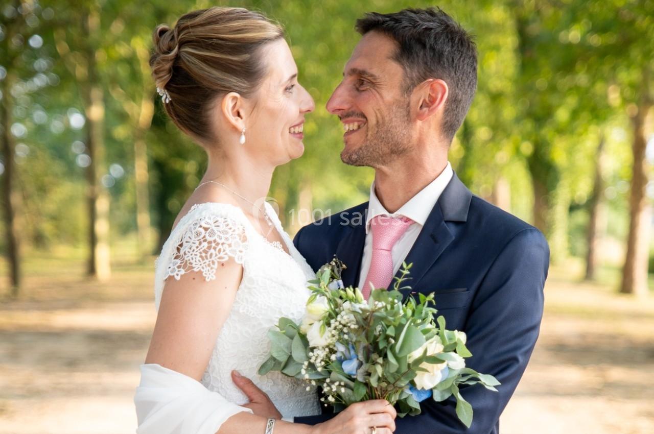 Un couple en tenue de mariage se regarde en souriant, debout dans un parc verdoyant.