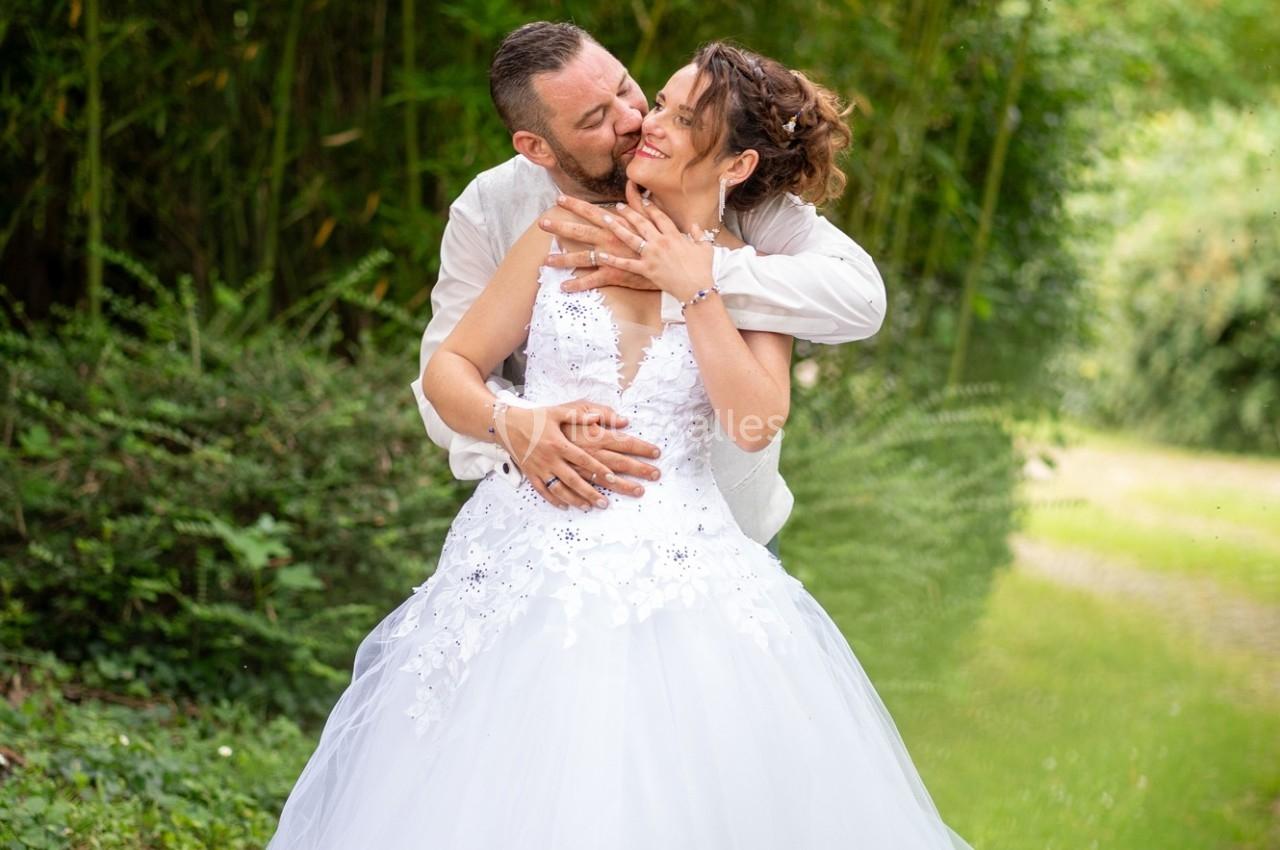 Un couple en tenue de mariage s'enlace dans un jardin verdoyant.