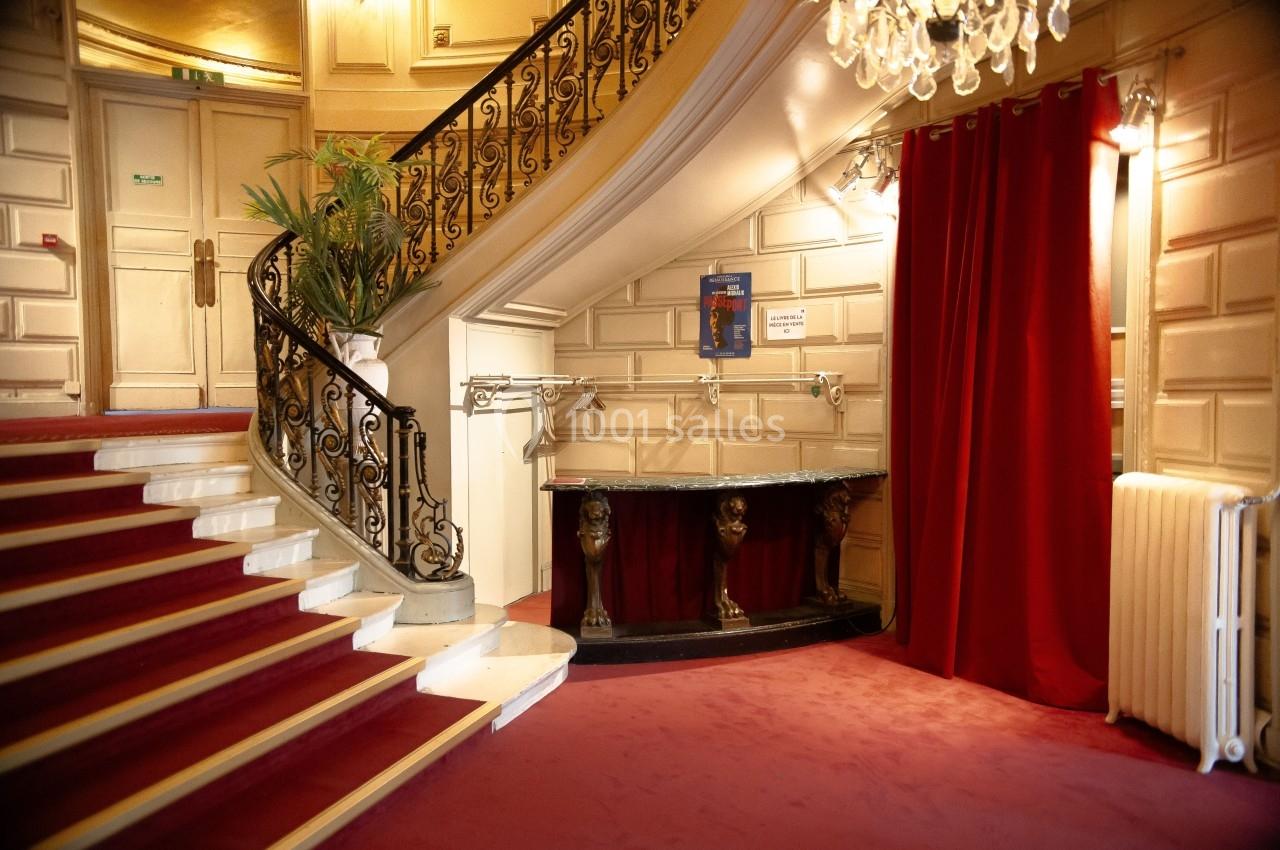 Escalier avec tapis rouge, rampe en fer forgé, rideaux rouges et comptoir décoratif dans un intérieur élégant.