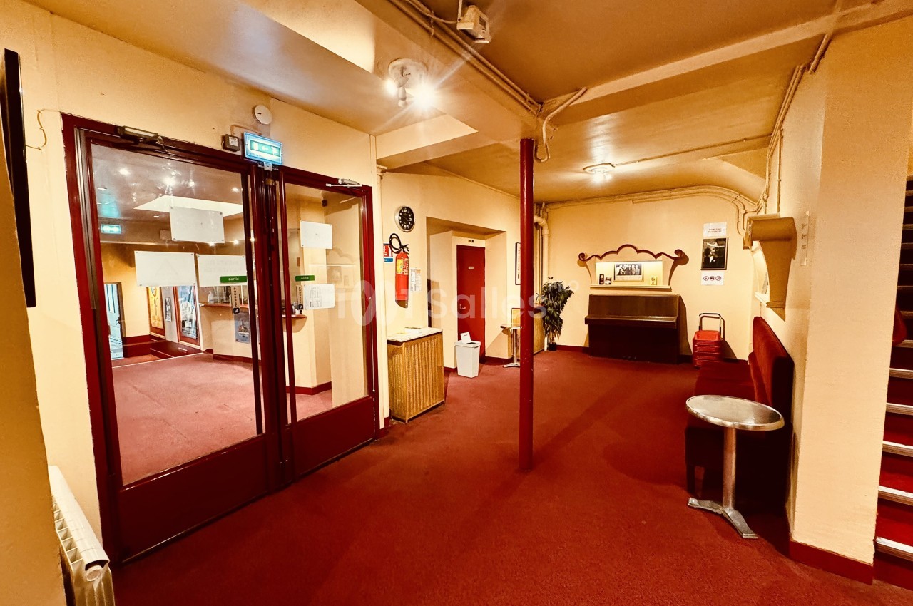 Couloir intérieur avec moquette rouge, portes vitrées, extincteur au mur et mobilier simple.