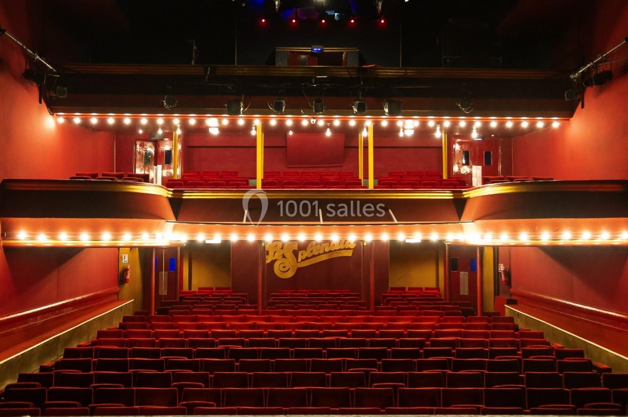 Vue depuis la scène d'un théâtre vide avec des rangées de sièges rouges et des balcons éclairés.