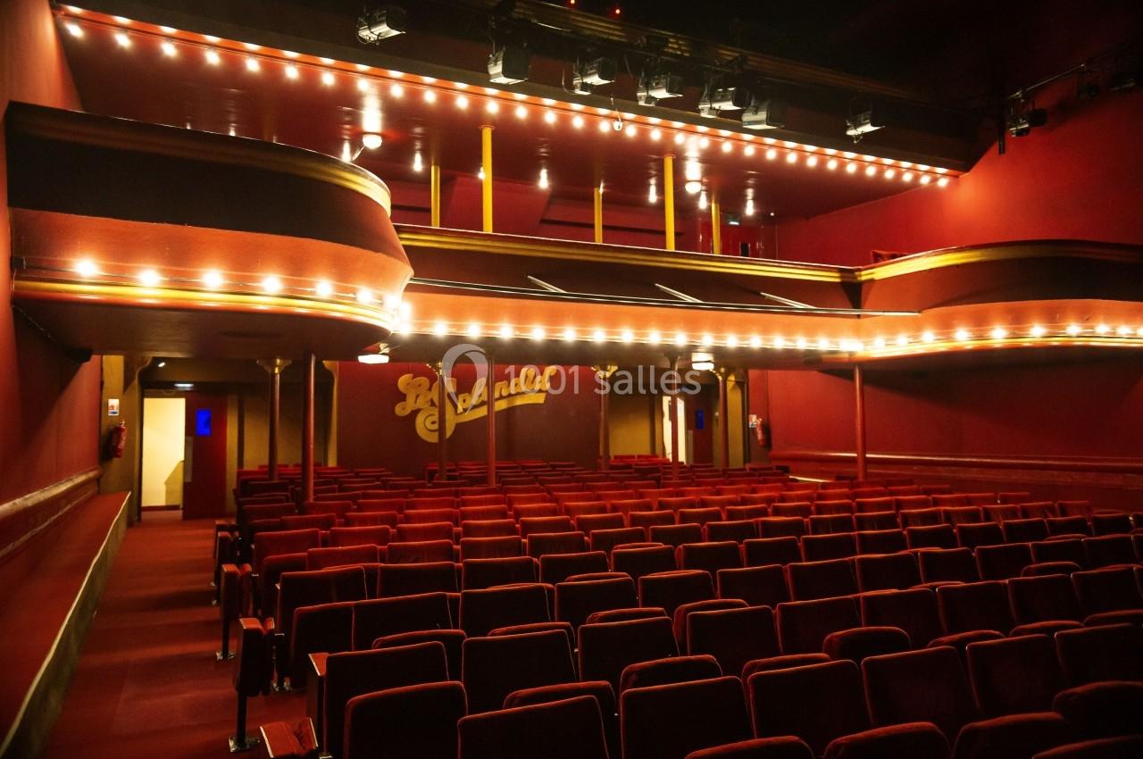 Salle de théâtre vide avec sièges rouges, balcons éclairés et enseigne lumineuse ’La Scalada’ au fond.