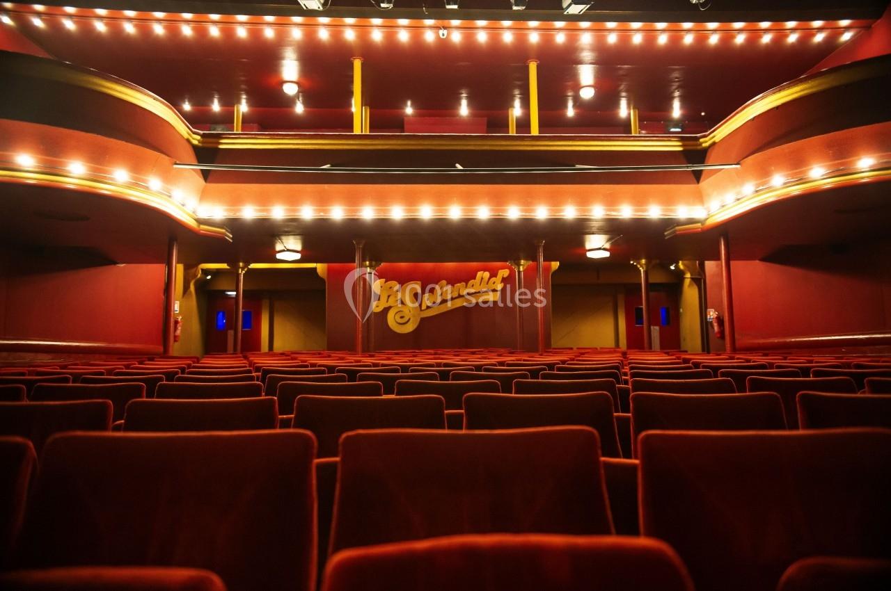 Salle de théâtre vide avec des rangées de fauteuils rouges et une scène ornée du nom ’Le Splendid’.
