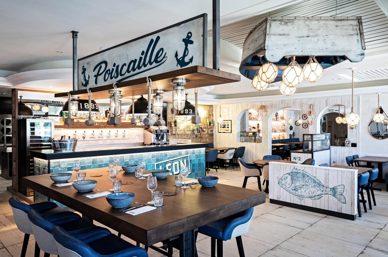 Salle de restaurant au décor marin avec tables dressées, comptoir en bois et éléments décoratifs nautiques.