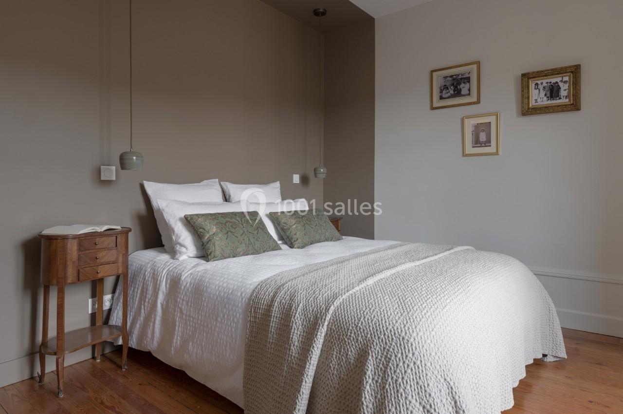 Lit double avec draps blancs, coussins décoratifs verts, tables de chevet en bois et cadres accrochés au mur beige.