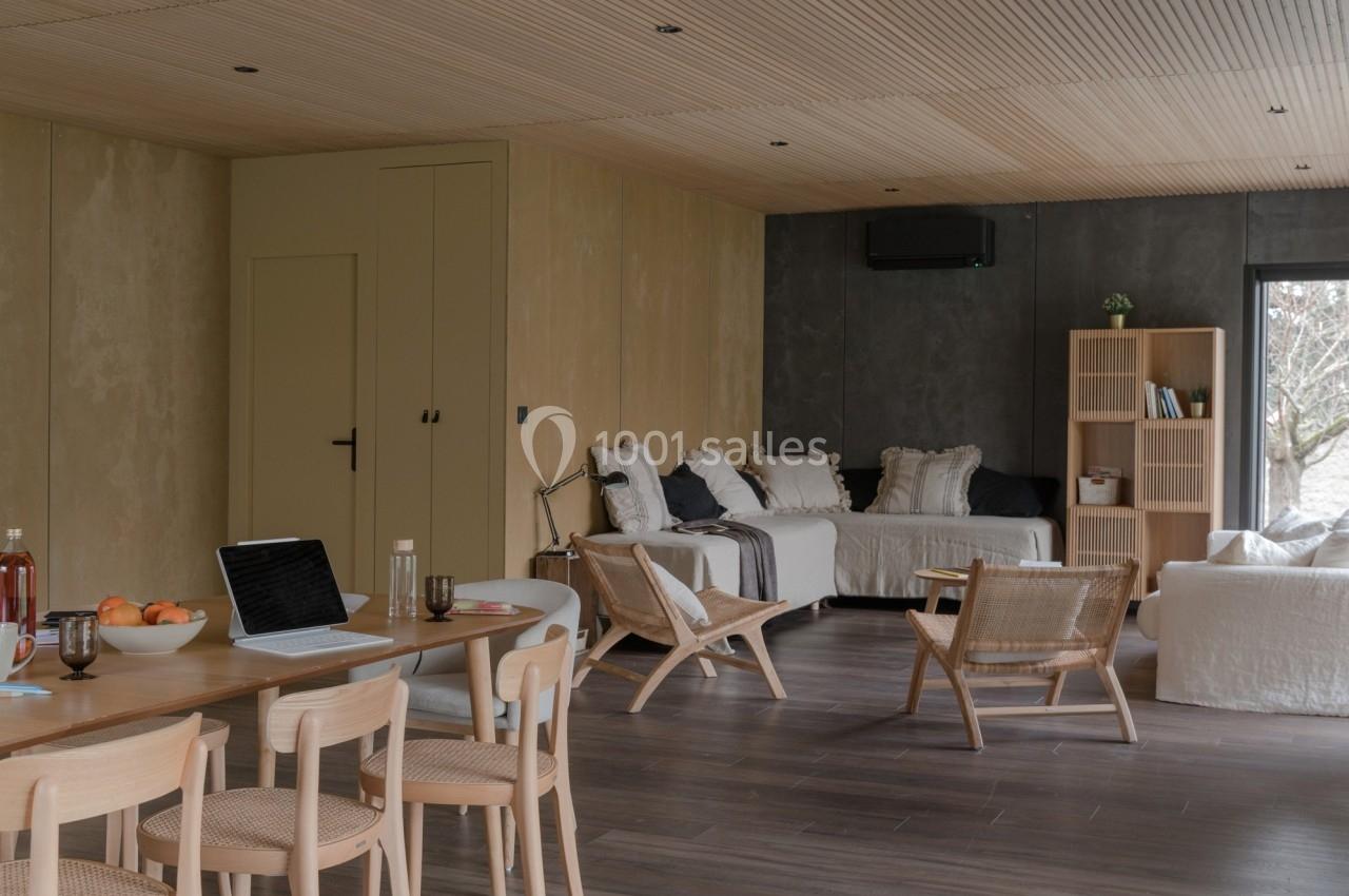 Salle de séjour lumineuse avec mobilier en bois clair, canapé blanc, étagères et table à manger équipée d'un ordinateur.