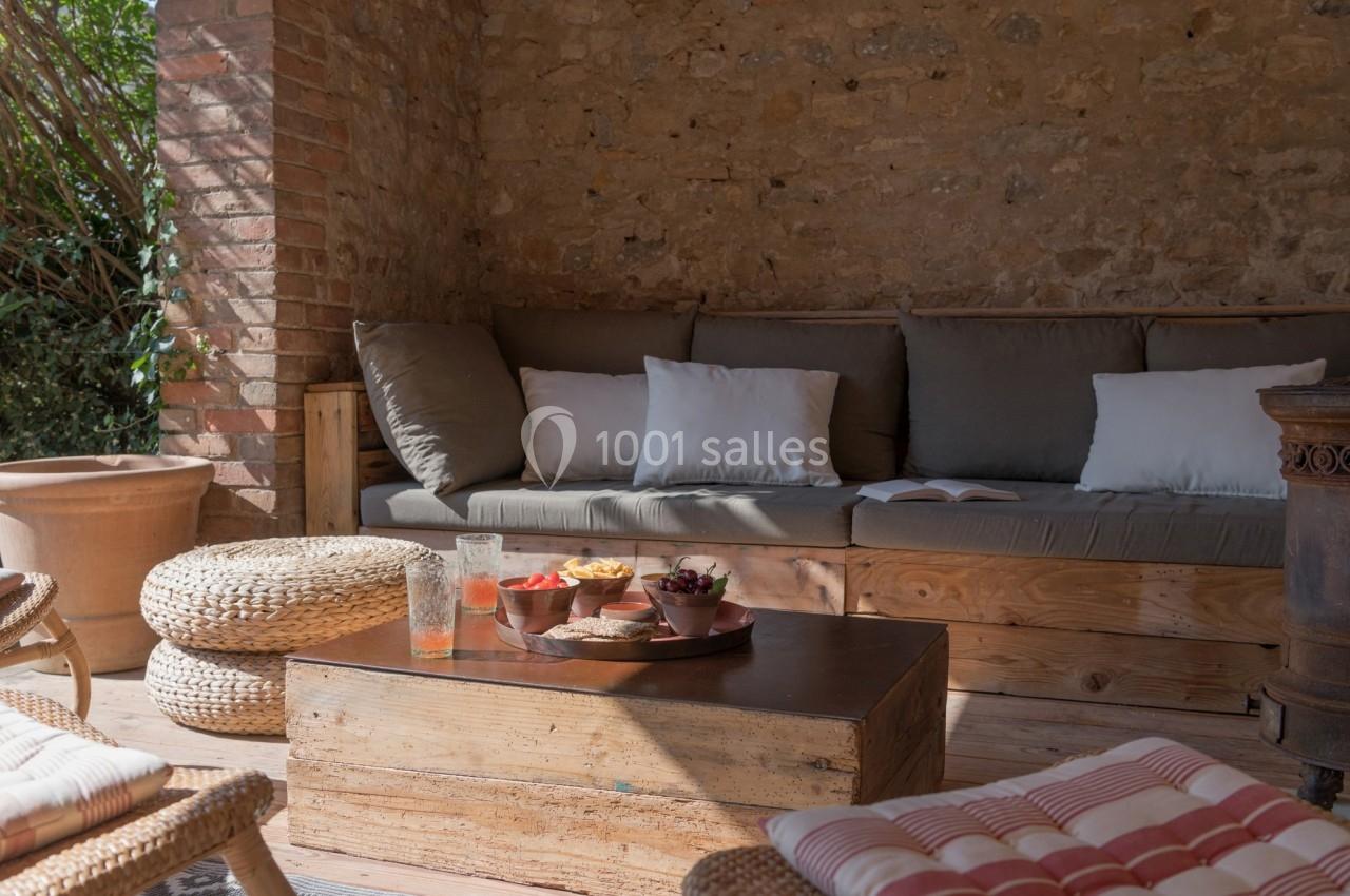 Terrasse en pierre avec canapé, coussins, table basse en bois et collations, éclairée par la lumière naturelle.