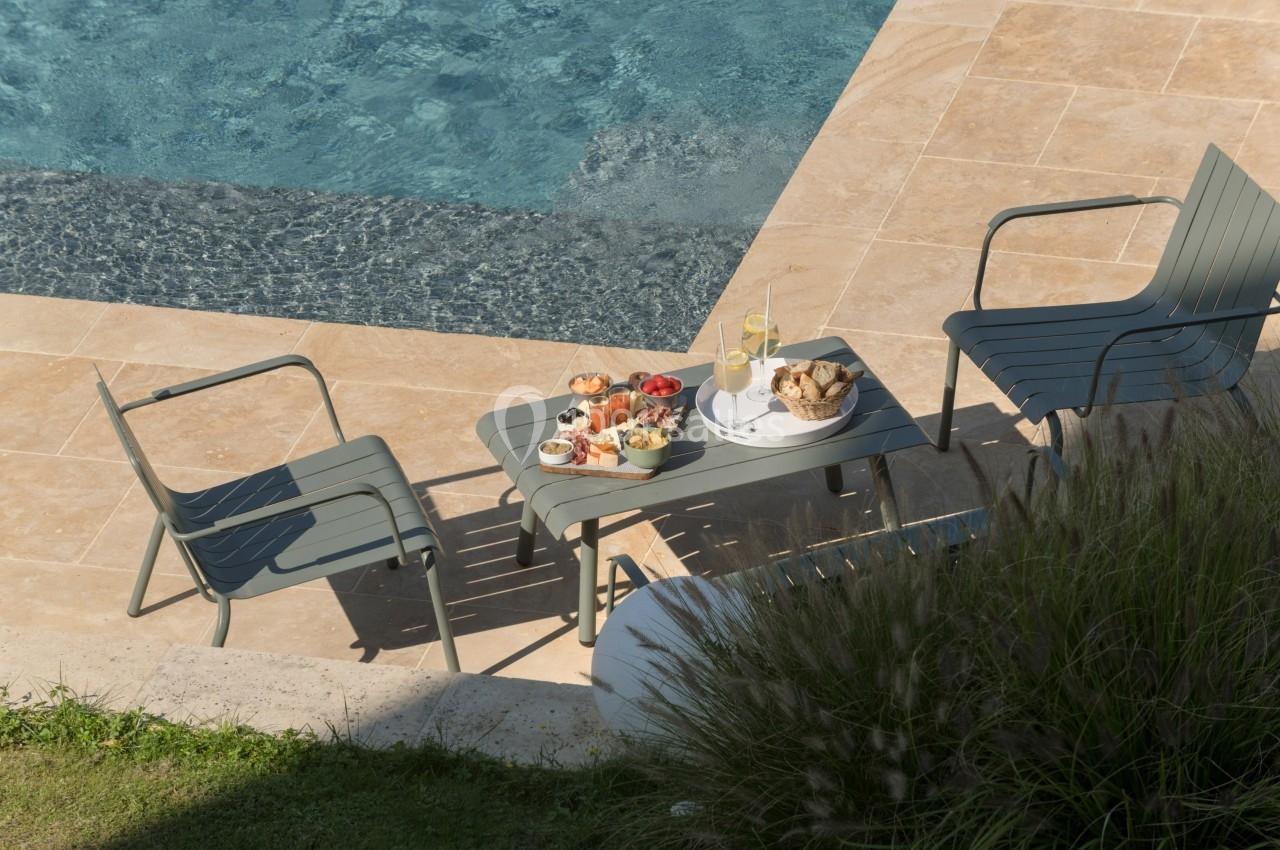 Table basse avec un petit-déjeuner composé de fruits, viennoiseries et jus, entourée de deux chaises près d'une piscine.