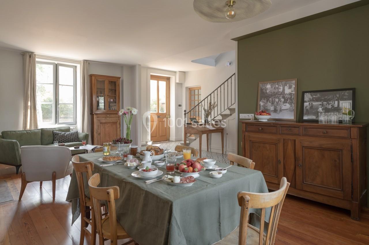 Salle à manger lumineuse avec table dressée pour le petit-déjeuner, meubles en bois et mur vert olive.