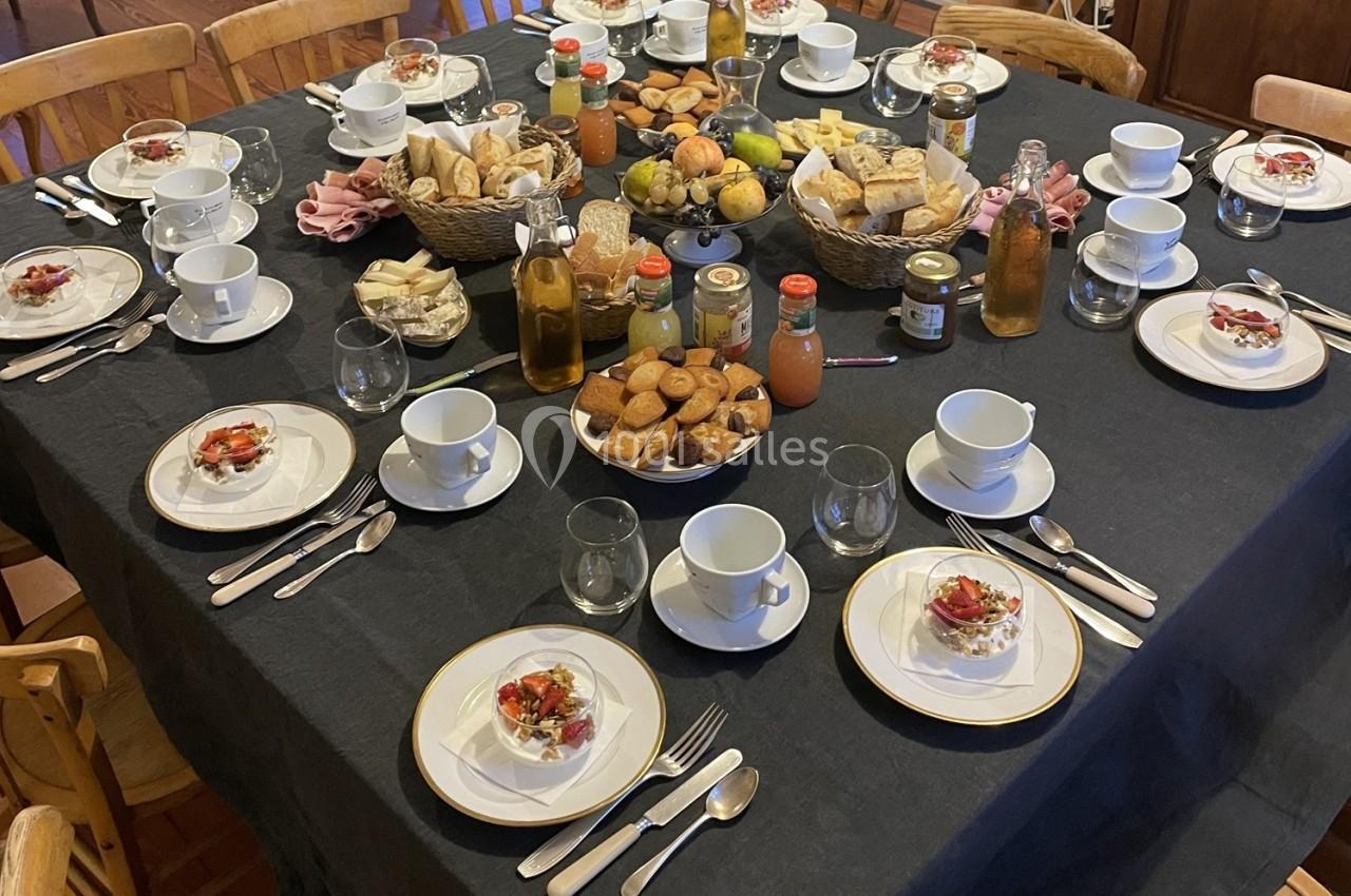 Table dressée pour un petit-déjeuner avec viennoiseries, fruits, boissons, et assiettes individuelles sur une nappe noire.