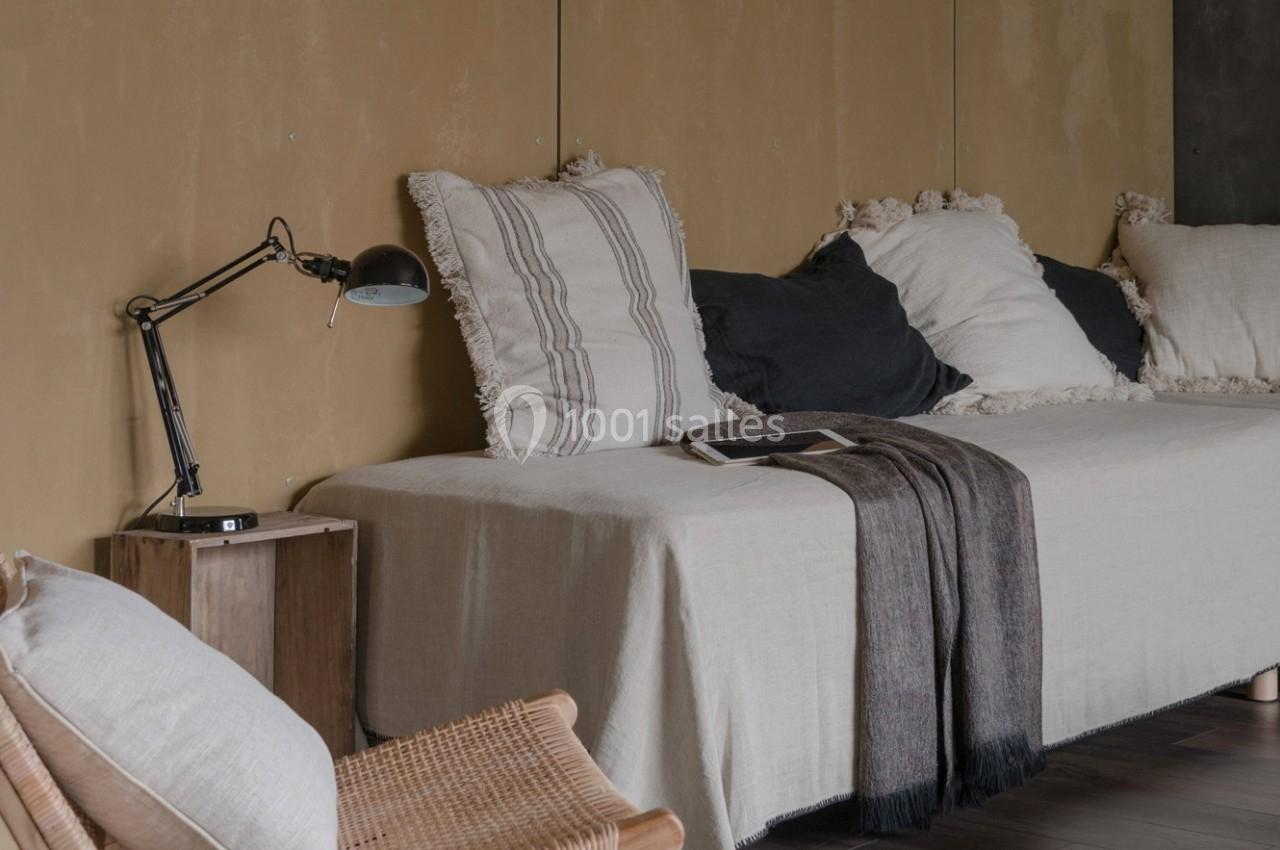 Canapé beige avec coussins décoratifs, plaid sombre et lampe de bureau noire sur une table en bois dans un intérieur…