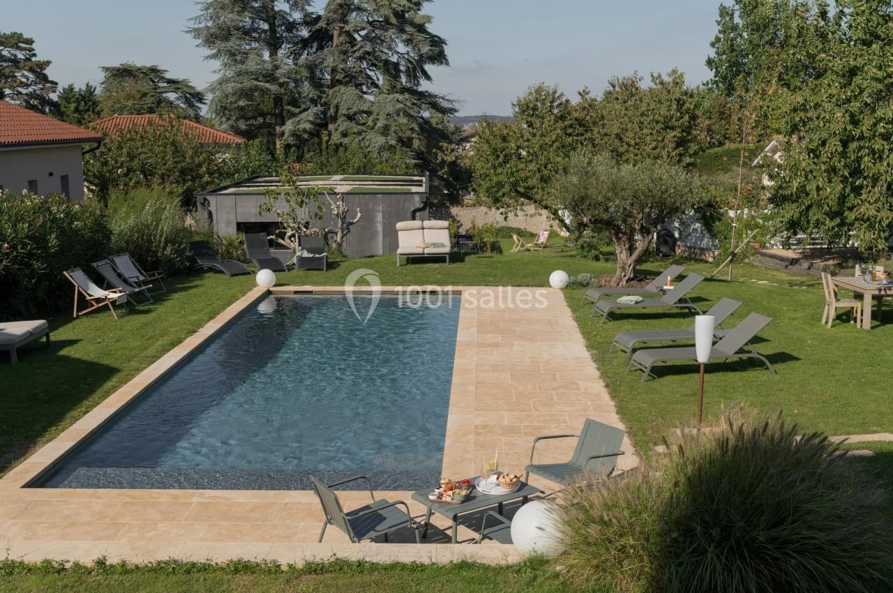 Piscine rectangulaire entourée de chaises longues, d'arbres et d'un jardin aménagé dans une propriété résidentielle.