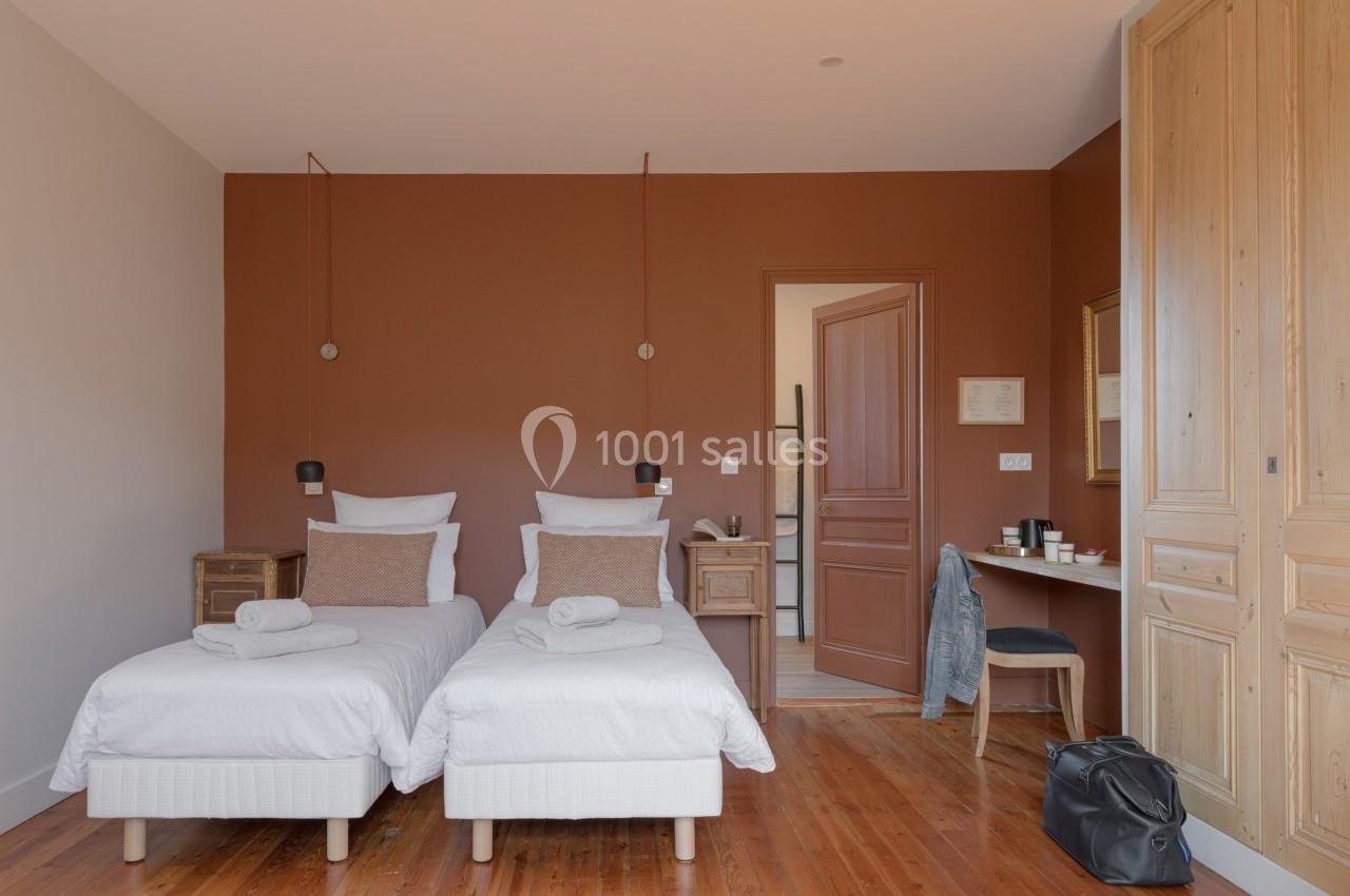 Chambre avec deux lits simples, murs marron, bureau avec chaise, armoire en bois et sol en parquet.