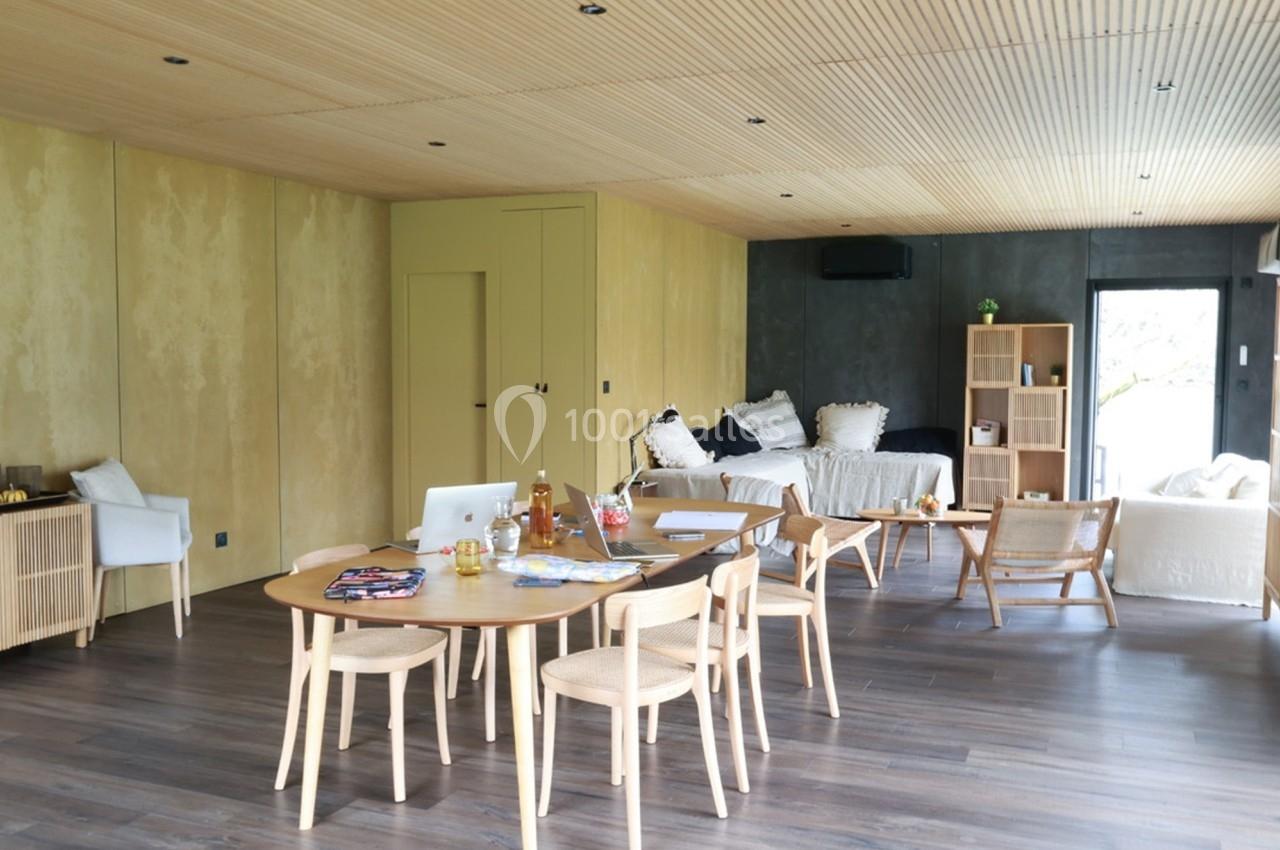 Salle de séjour lumineuse avec table en bois, chaises, canapé, lit, étagères et décoration minimaliste.