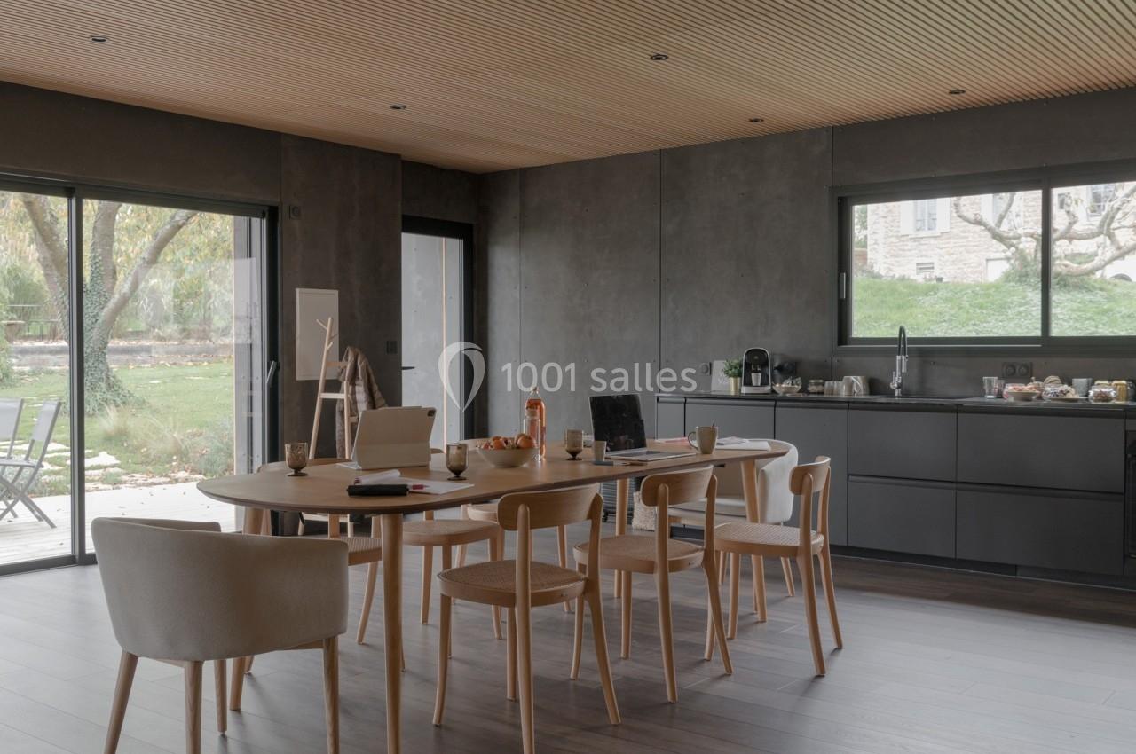 Salle à manger moderne avec table en bois, chaises assorties, cuisine ouverte et vue sur un jardin par de grandes baies…