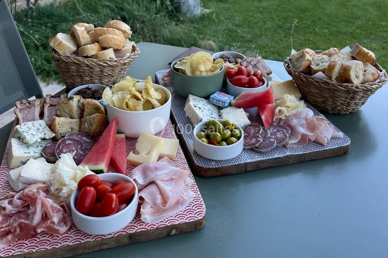 Plateaux garnis de charcuteries, fromages, olives, tomates cerises, chips et pain, disposés sur une table en extérieur.