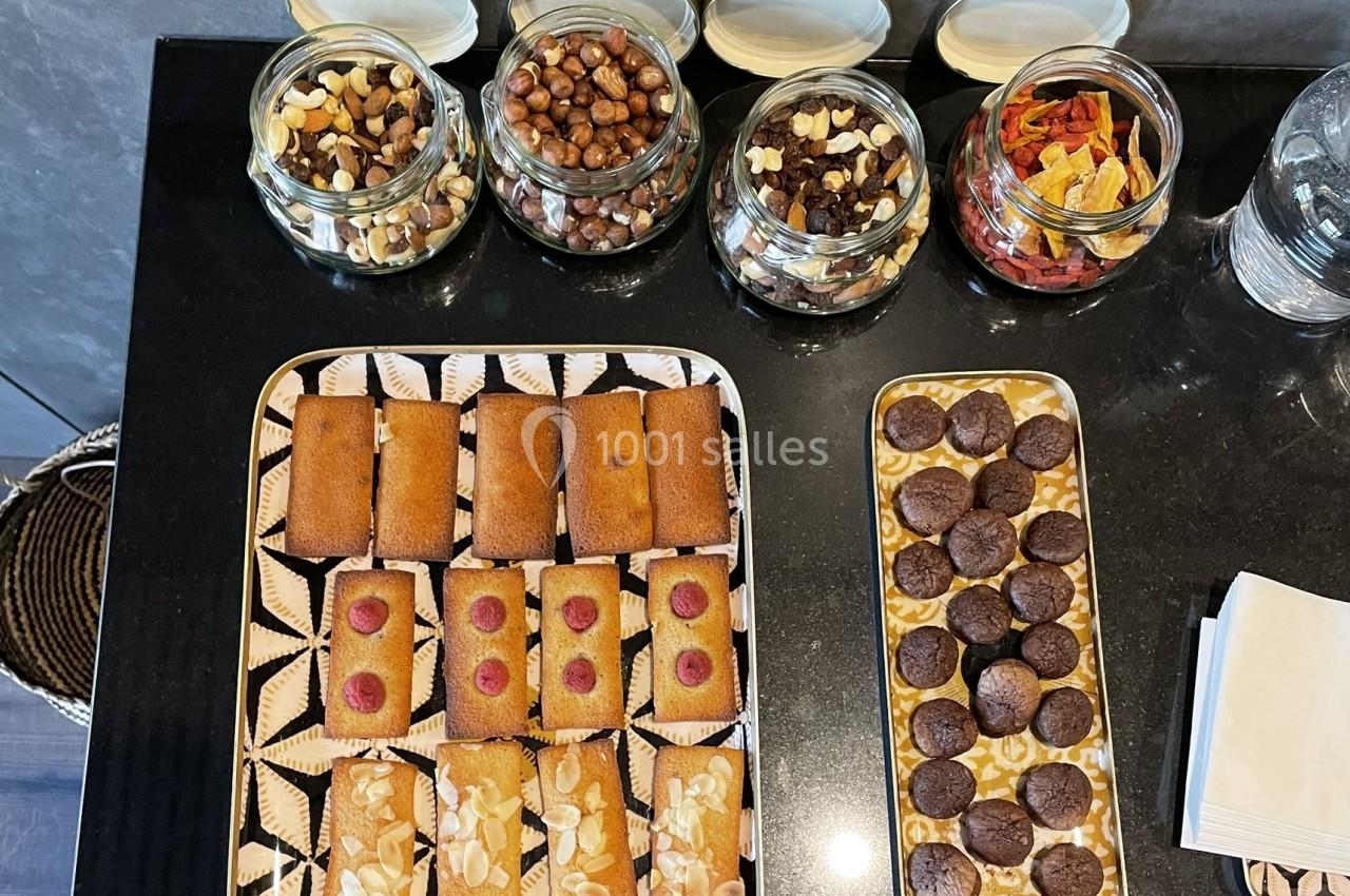Plateaux de financiers aux amandes et framboises, mini-brownies, avec des bocaux de fruits secs en arrière-plan.