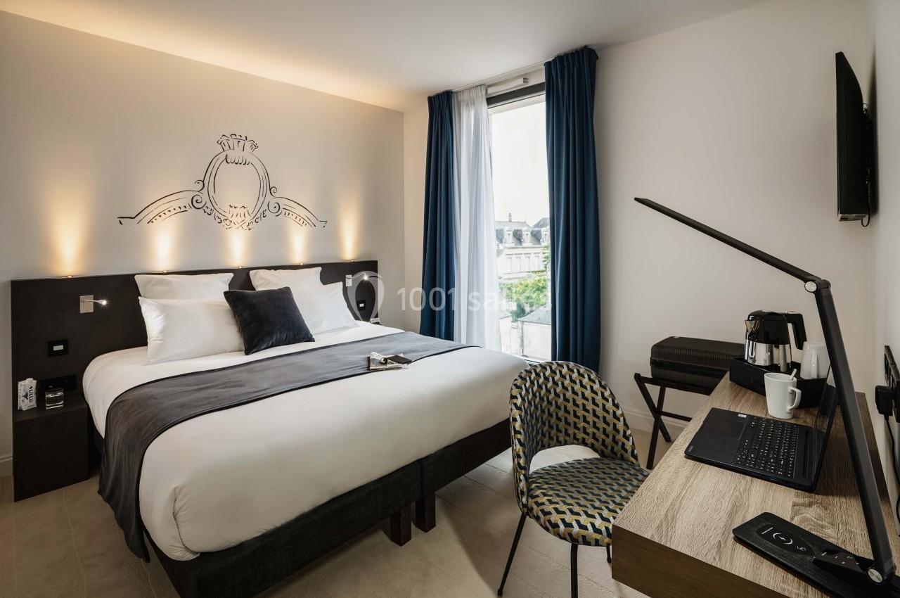 Chambre d'hôtel moderne avec lit double, bureau équipé, chaise, machine à café et fenêtre donnant sur l'extérieur.