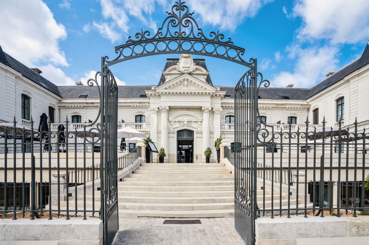 Entrée principale d'un bâtiment historique avec escalier en pierre, portail en fer forgé et façade élégante.