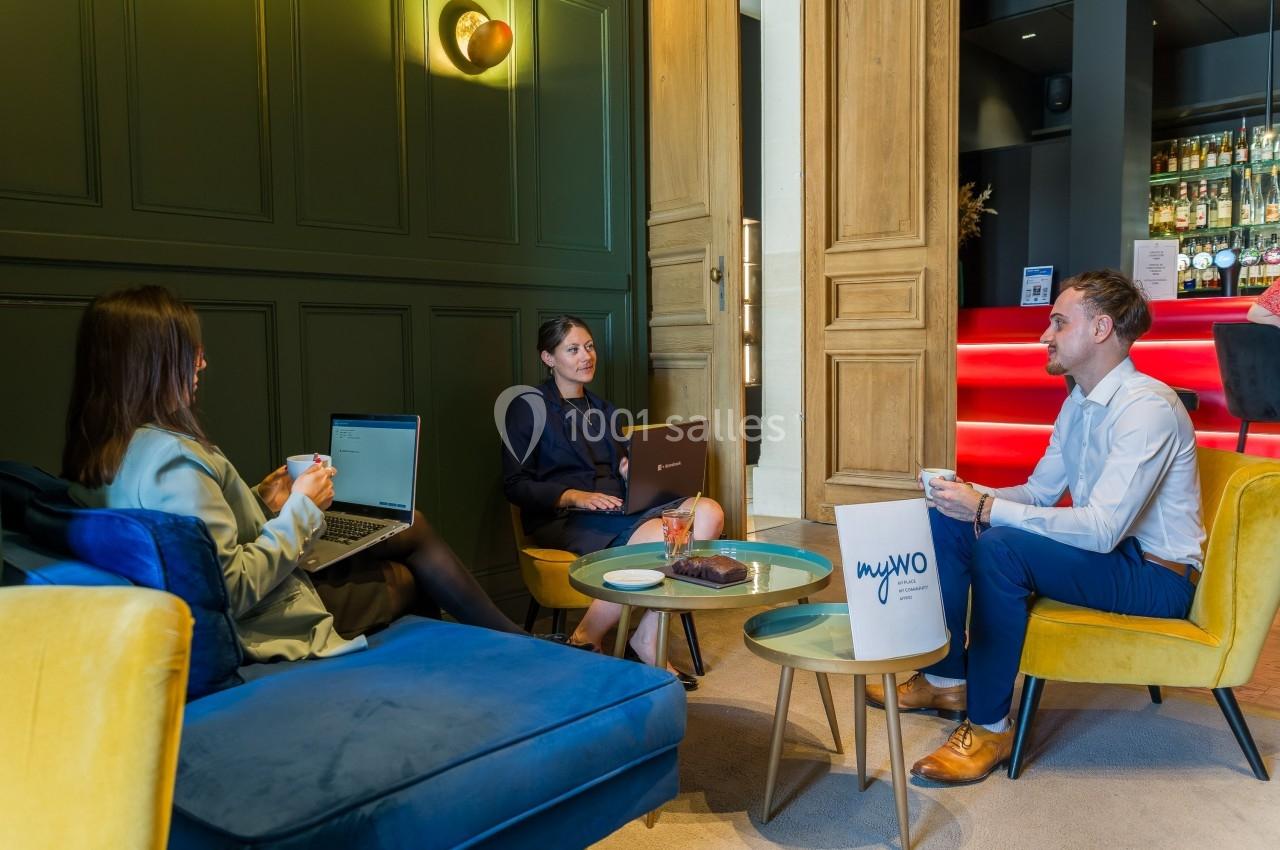 Trois personnes discutent autour d'une table basse dans un espace lounge moderne avec fauteuils et éclairage chaleureux.