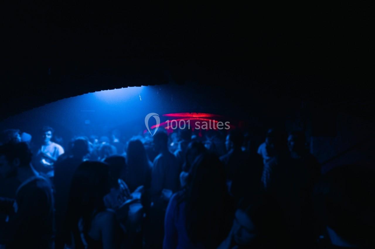 Foule dans une ambiance sombre avec éclairage bleu et rouge, probablement dans un club ou une salle de concert.