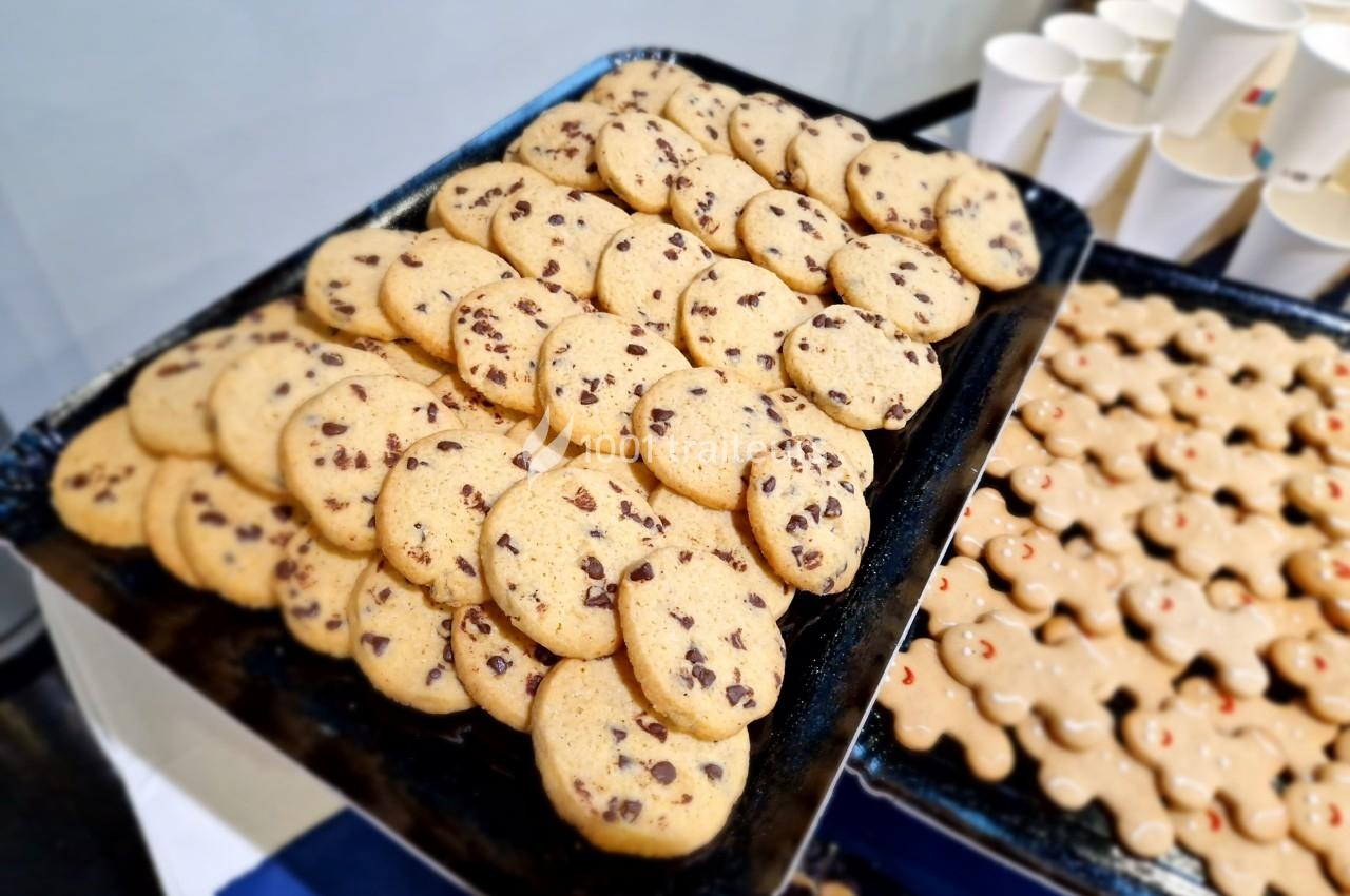 Plateau de biscuits aux pépites de chocolat et de biscuits en forme de bonhommes, disposés près de gobelets blancs.