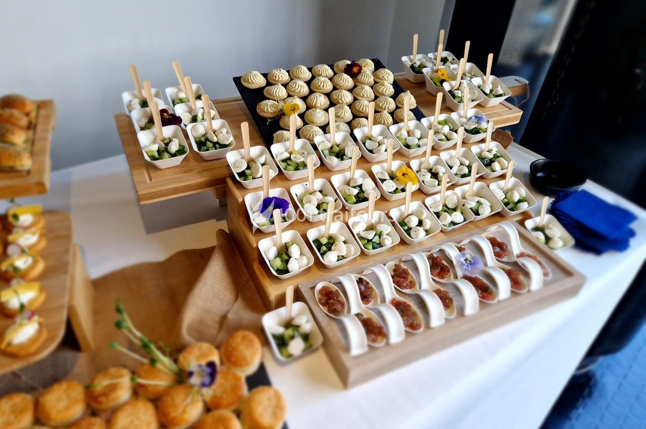Plateau de buffet avec des amuse-bouches variés, disposés sur des présentoirs en bois, incluant brochettes et mini…