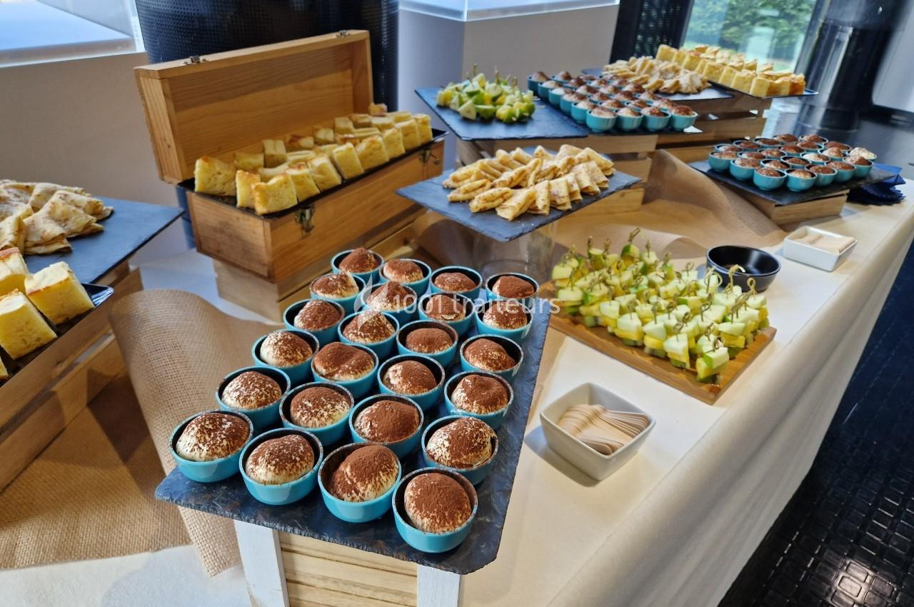 Buffet avec desserts individuels, verrines de tiramisu, parts de gâteau et brochettes de fruits sur une table.