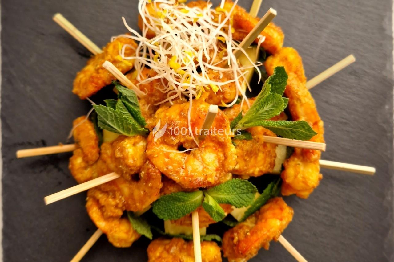 Brochettes de crevettes dorées garnies de feuilles de menthe et de pousses germées, présentées sur une ardoise.