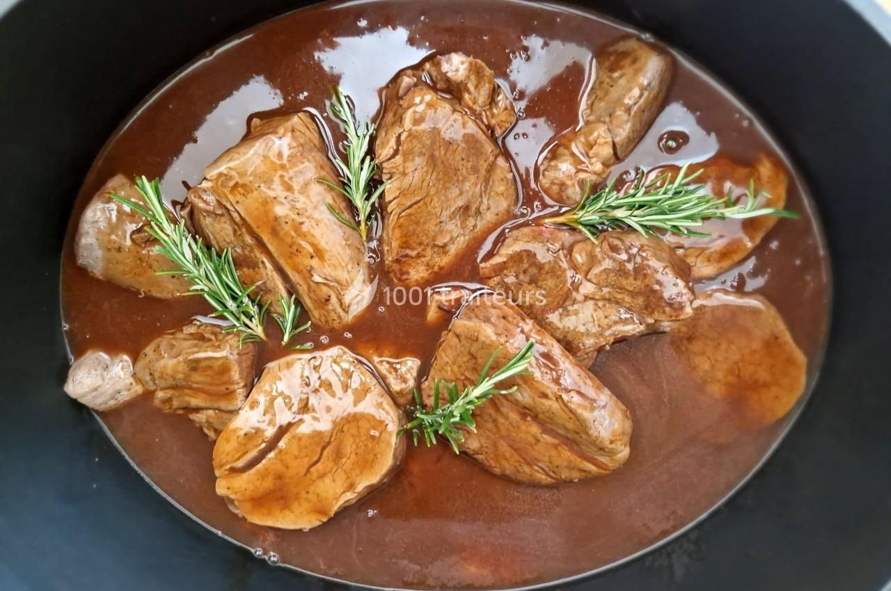 Morceaux de viande mijotés dans une sauce brune, garnis de brins de romarin, présentés dans une cocotte noire.