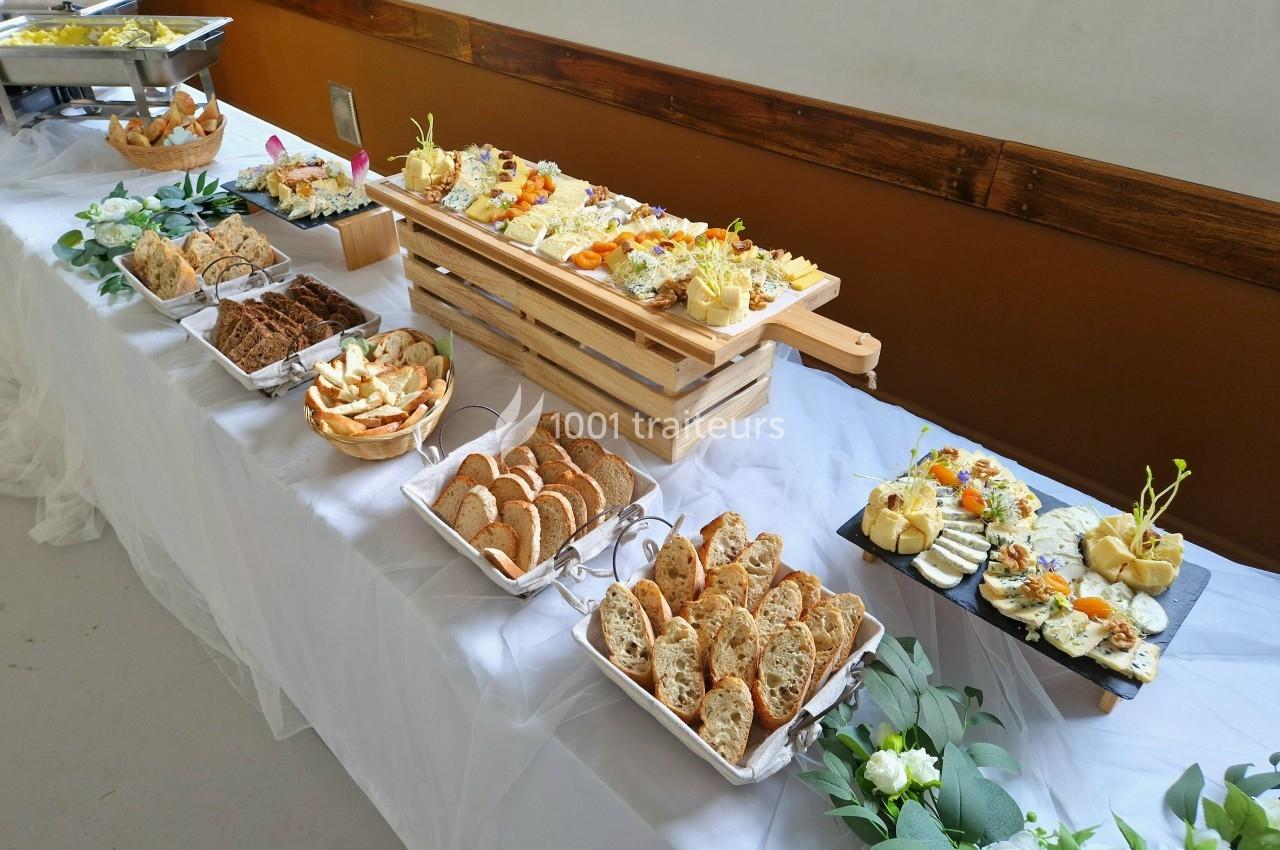 Buffet avec divers plats froids, pains, fromages et décorations florales sur une table blanche.