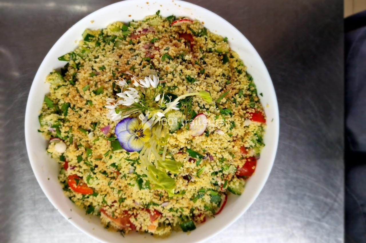 Salade de couscous garnie de légumes frais, herbes et fleurs comestibles, présentée dans un bol blanc.