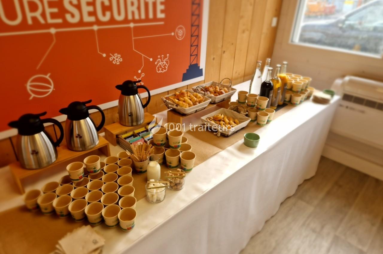 Table de buffet avec thermos de café, viennoiseries, jus, tasses en carton et accessoires pour boissons chaudes.