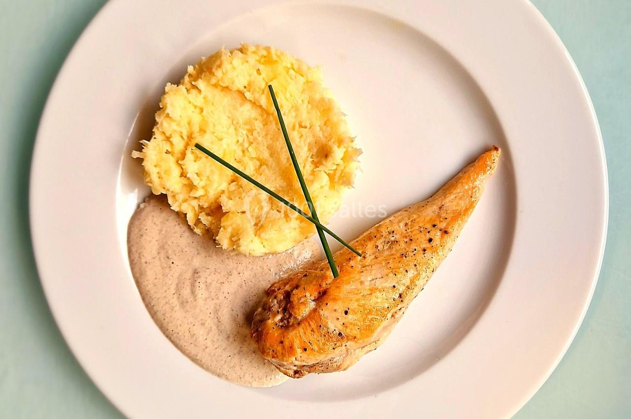 Assiette avec filet de poulet grillé, purée de pommes de terre, sauce crémeuse et brins de ciboulette en décoration.