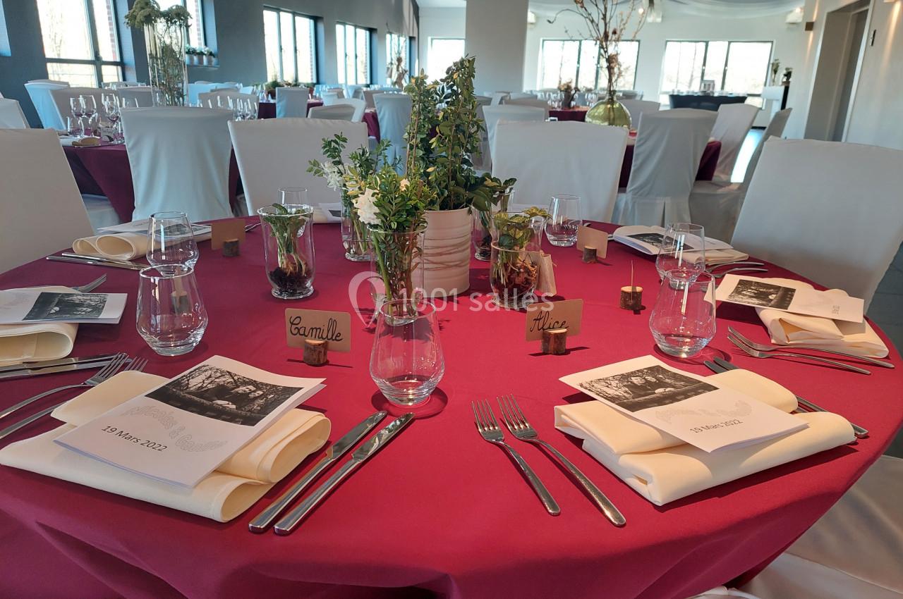 Table de réception décorée avec nappes rouges, vaisselle élégante, menus personnalisés et centre de table floral.